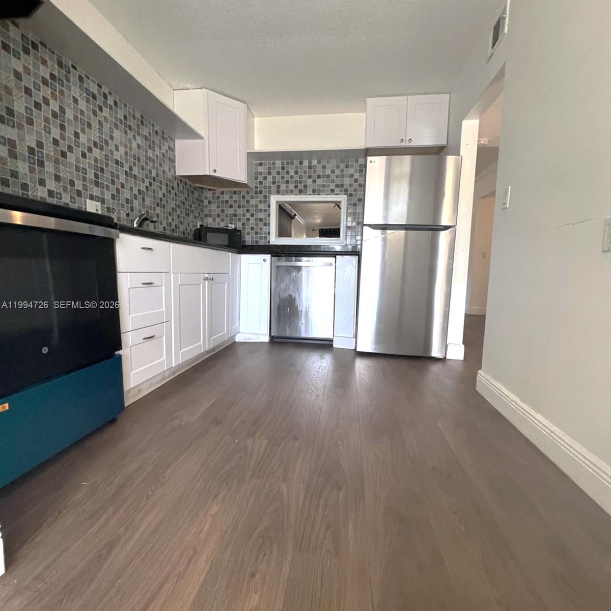A kitchen features white cabinets, stainless steel appliances, a mosaic tile backsplash, and wood flooring — 109 SW 1st Ave, Hallandale Beach FL 33009, HALLANDALE BEACH, FL