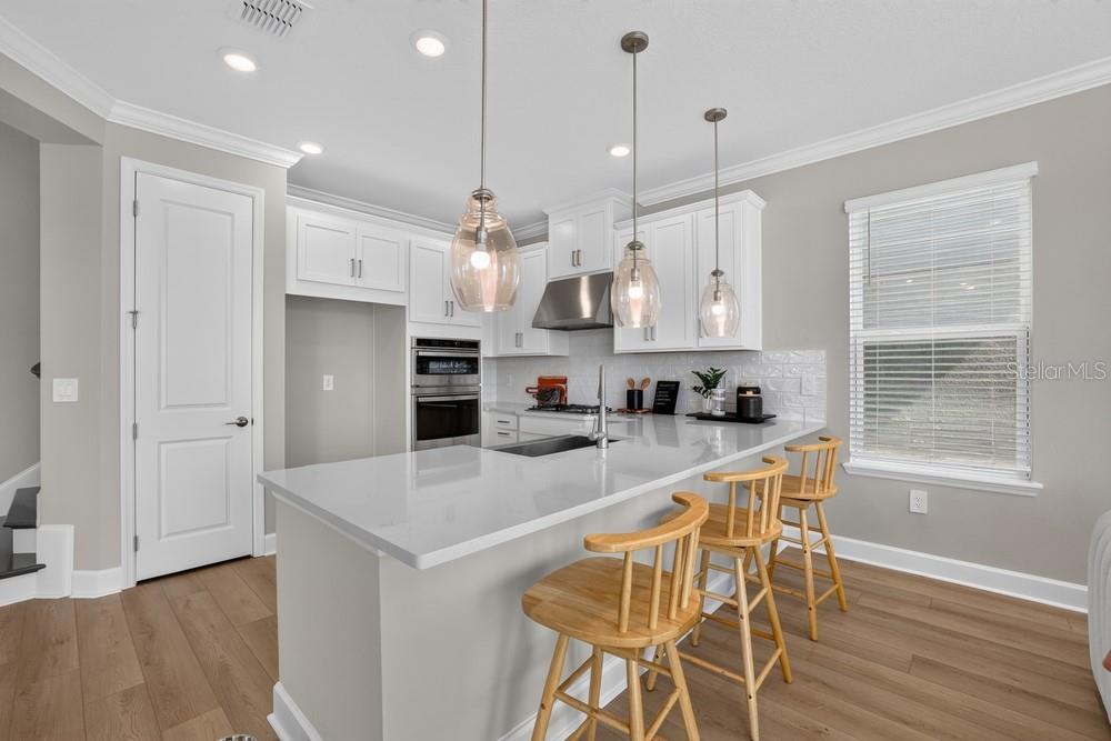 A modern kitchen features white cabinetry, a quartz island with bar seating, and stainless appliances — 5073 LOST KEY PLACE, ST CLOUD, FL