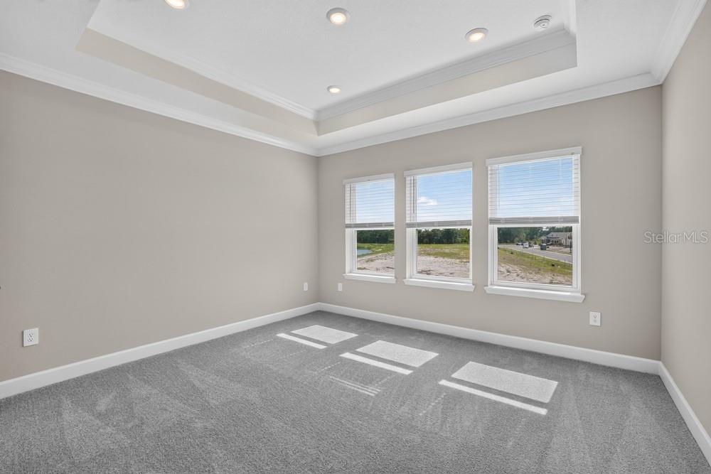 An empty bedroom with gray carpet, a tray ceiling, and three windows overlooking a field — 5073 LOST KEY PLACE, ST CLOUD, FL