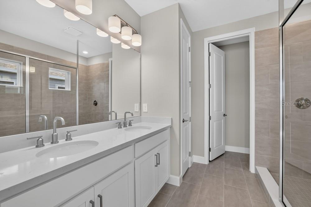 A bathroom features a double vanity with white cabinets, a large mirror, and a tiled shower — 5073 LOST KEY PLACE, ST CLOUD, FL