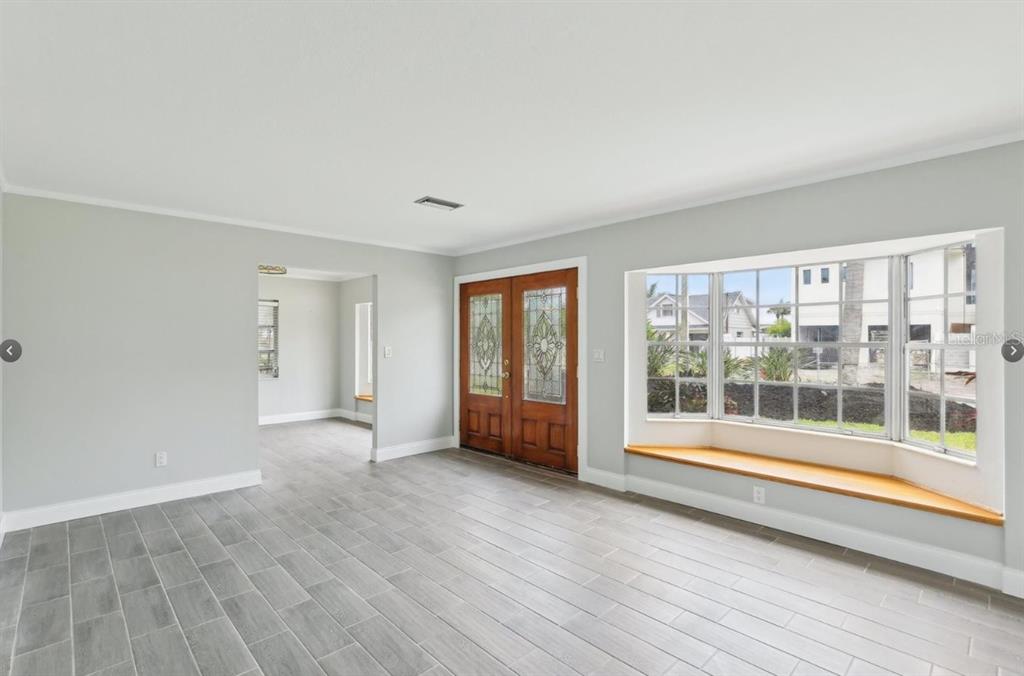 A living room with gray tile floors, a wooden bay window seat, and double front doors — 8706 ELMWOOD LANE, TAMPA, FL