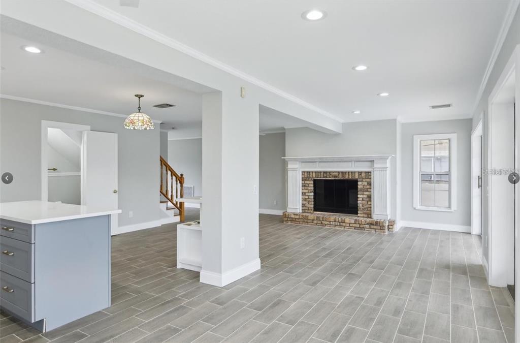 A bright living room with a brick fireplace, gray tile flooring, and a kitchen island — 8706 ELMWOOD LANE, TAMPA, FL