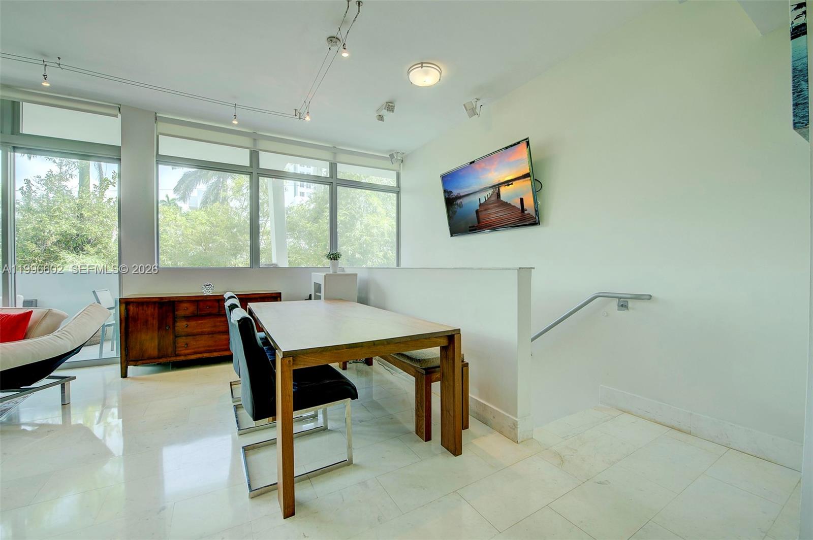 A dining area features a wooden table, chairs, a sideboard, and a wall-mounted television — 1577 Bay Rd # 201, Miami Beach FL 33139, MIAMI BEACH, FL