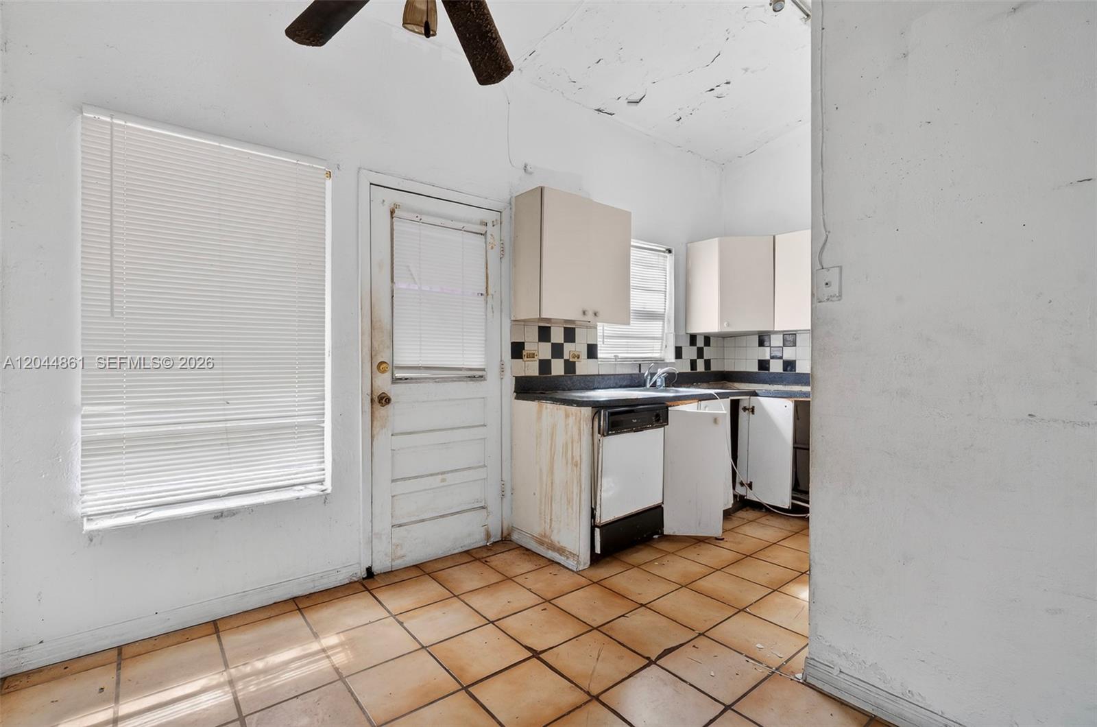 A kitchen features tiled floors, white cabinets, a dishwasher, and a door to the outside — MIAMI, FL