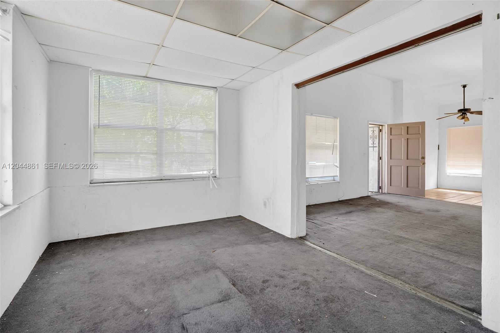 An interior view shows two connected rooms with gray carpeting, white walls, and drop ceilings — MIAMI, FL
