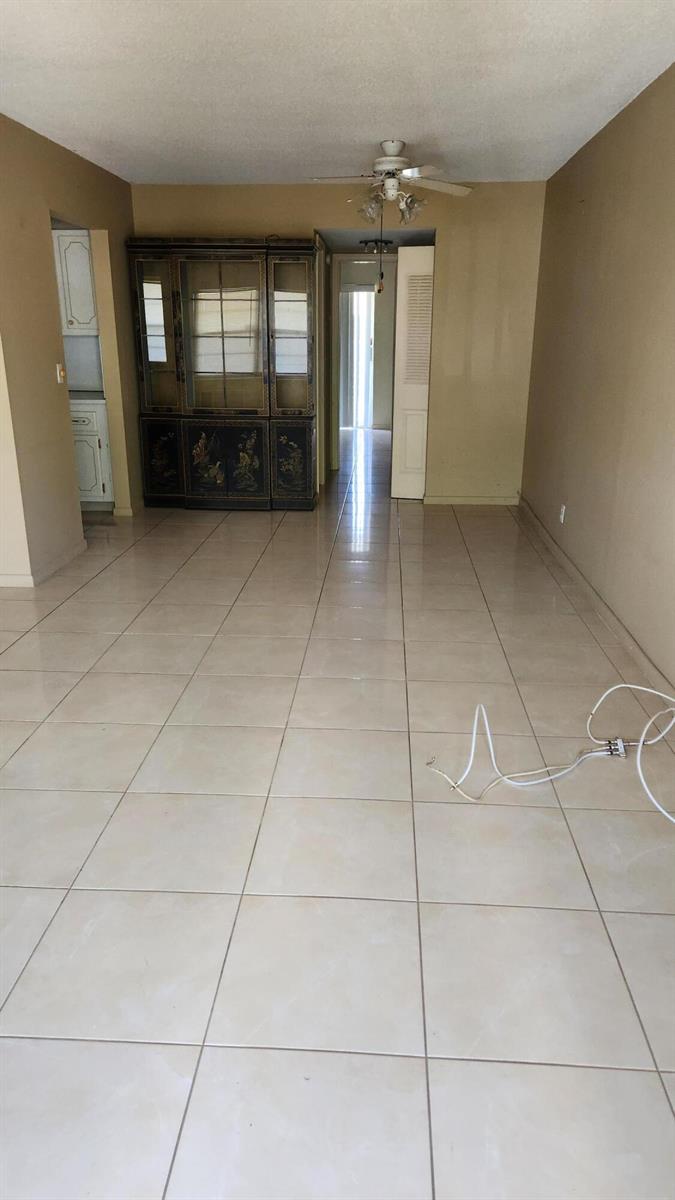 An empty room with light-colored floor tiles, a ceiling fan, and a dark wood hutch — 102 Andover D, West Palm Beach FL 33417, WEST PALM BEACH, FL