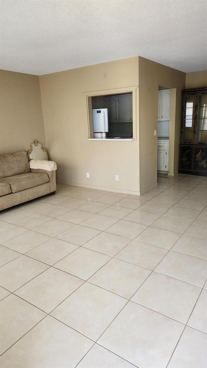 A living room with beige walls, tile flooring, a tan sofa, and a kitchen pass-through — 102 Andover D, West Palm Beach FL 33417, WEST PALM BEACH, FL