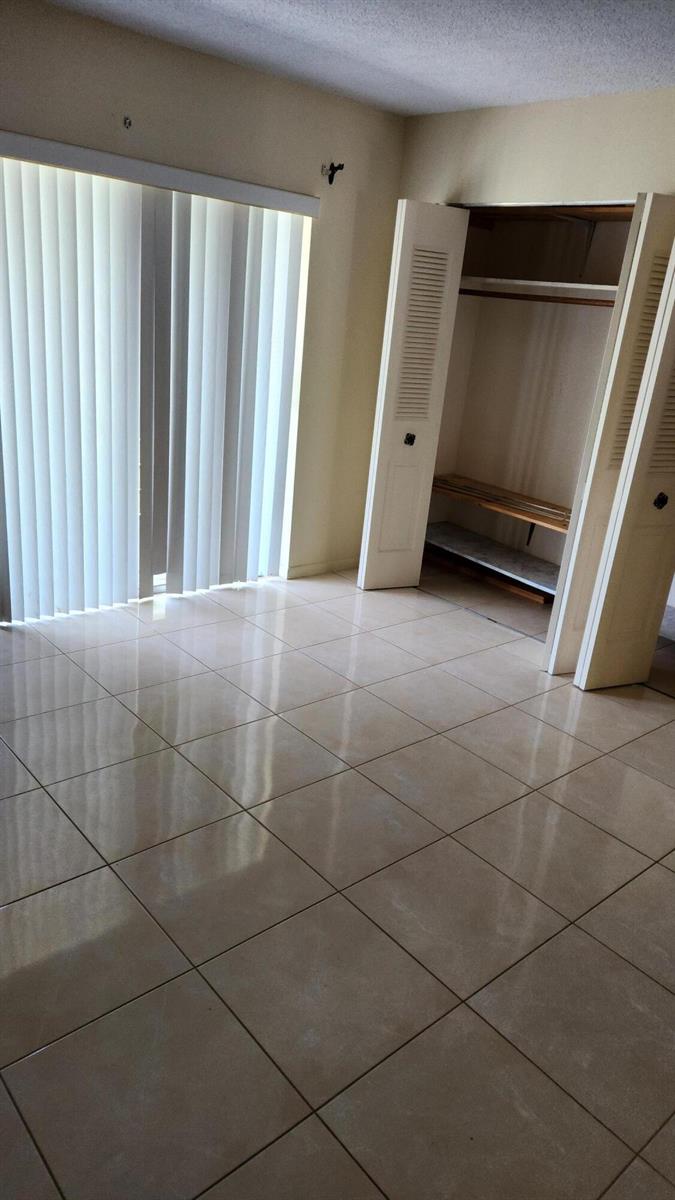 An empty room features light-colored floor tiles, a sliding glass door, and an open closet — 102 Andover D, West Palm Beach FL 33417, WEST PALM BEACH, FL