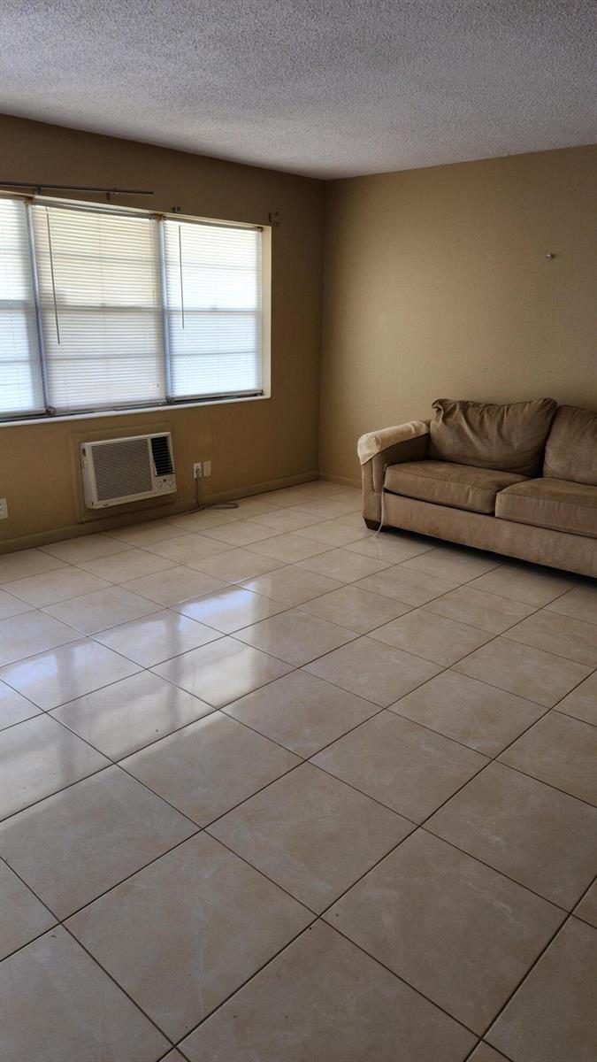 A living room with beige tile flooring, tan walls, a window with blinds, and a sofa — 102 Andover D, West Palm Beach FL 33417, WEST PALM BEACH, FL