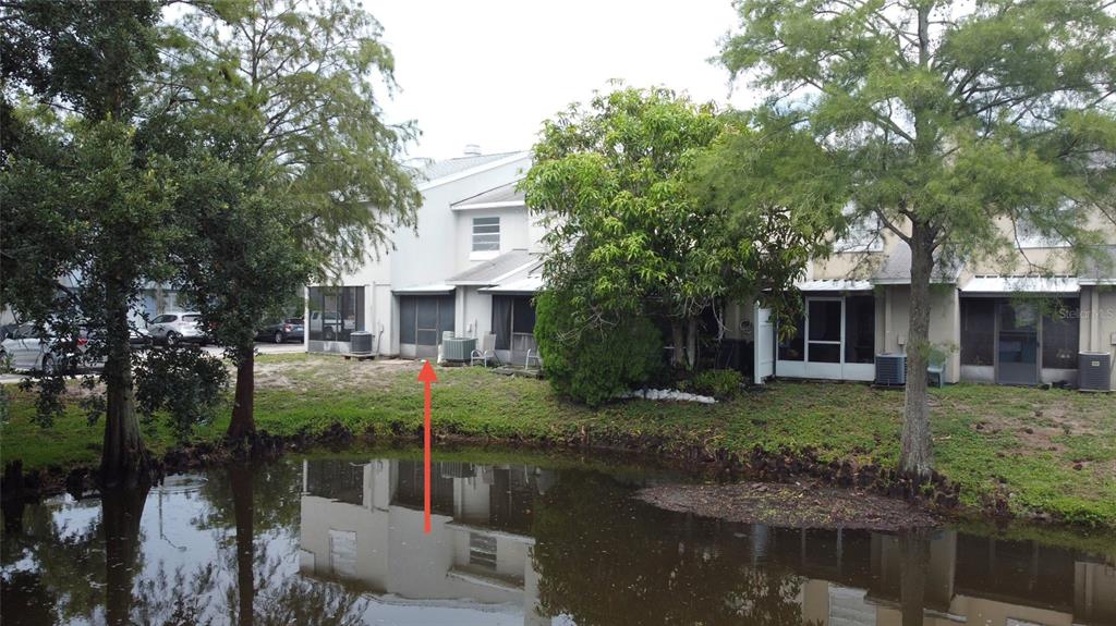 The rear exterior of a multi-story townhouse features a screened patio overlooking a small pond — 6661 121ST AVENUE UNIT G, LARGO, FL