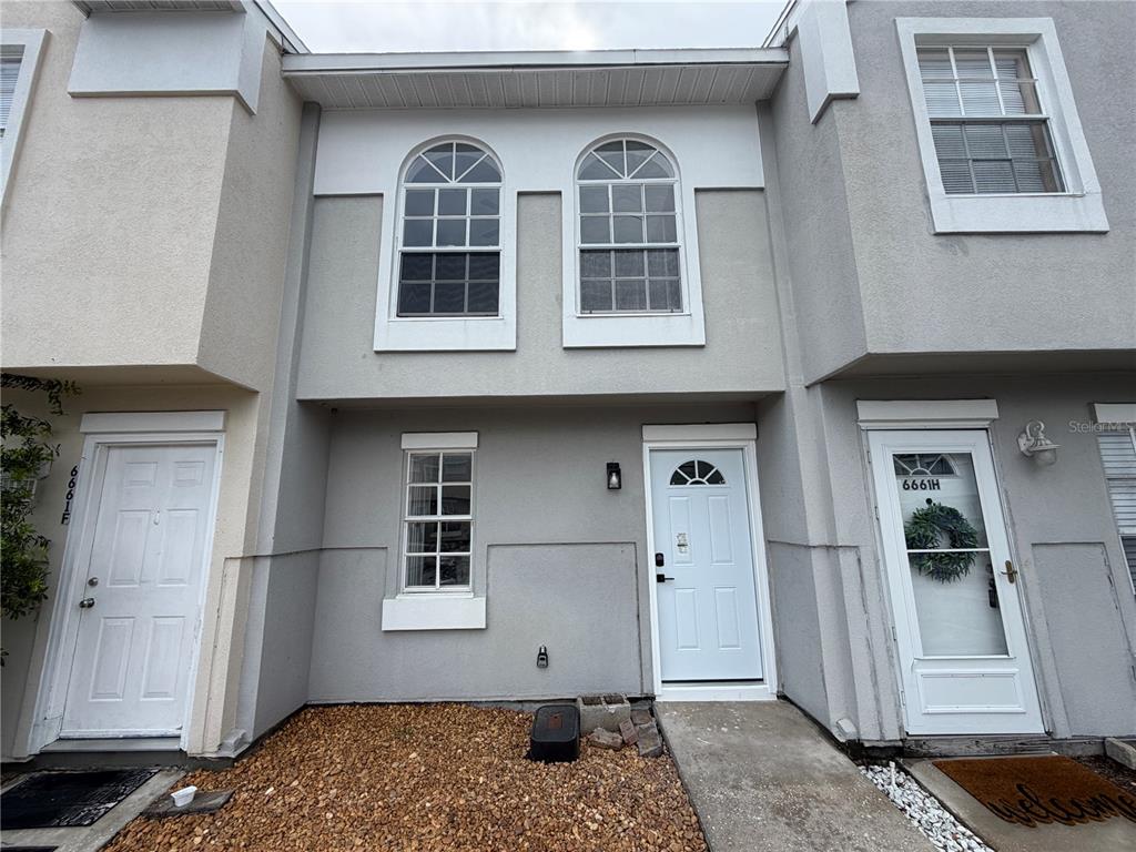 A two-story townhouse exterior with gray stucco walls, arched windows, and three white doors — 6661 121ST AVENUE UNIT G, LARGO, FL