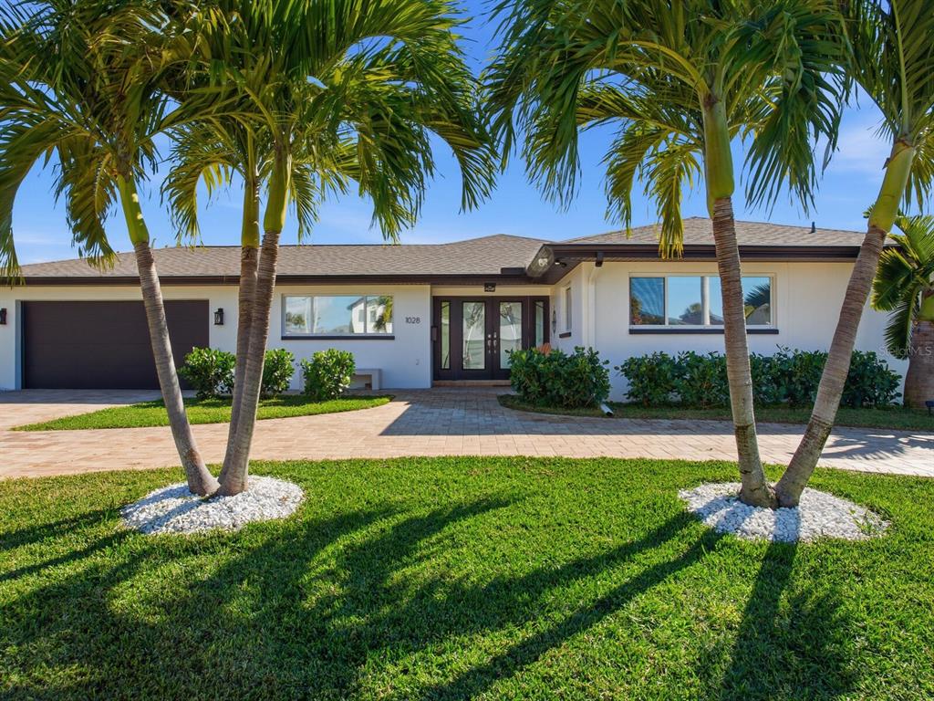 A single-story house with a paved driveway, palm trees, and a dark-framed front entrance — 1028 79TH STREET S, ST PETERSBURG, FL