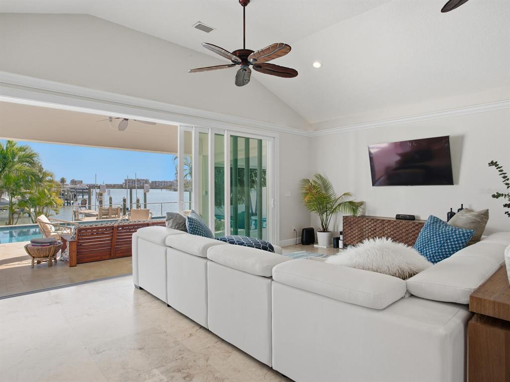 A living room with a white sectional sofa, vaulted ceiling, and sliding doors opening to a waterfront patio — 1028 79TH STREET S, ST PETERSBURG, FL