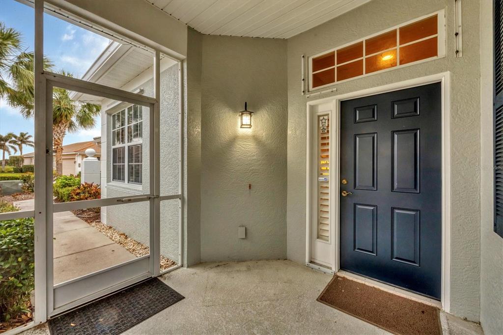 A covered entryway features a dark blue front door, a screen door, and a wall sconce — 1647 LANCASHIRE DRIVE UNIT 1647, VENICE, FL