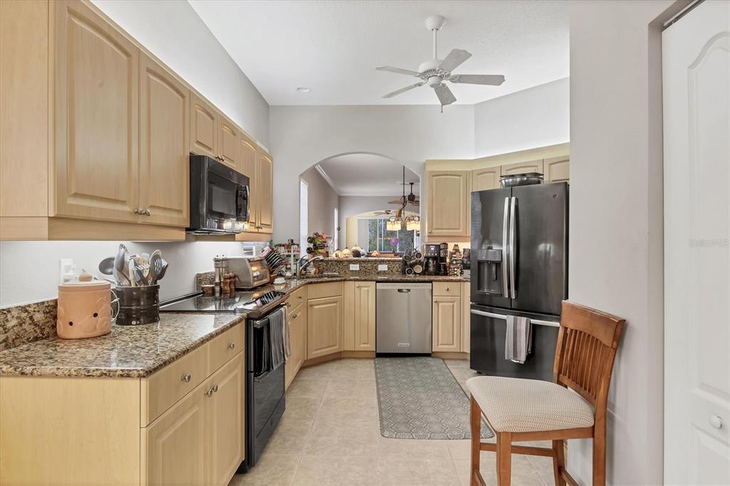 A kitchen features light wood cabinets, granite countertops, stainless steel appliances, and a black refrigerator — 1647 LANCASHIRE DRIVE UNIT 1647, VENICE, FL