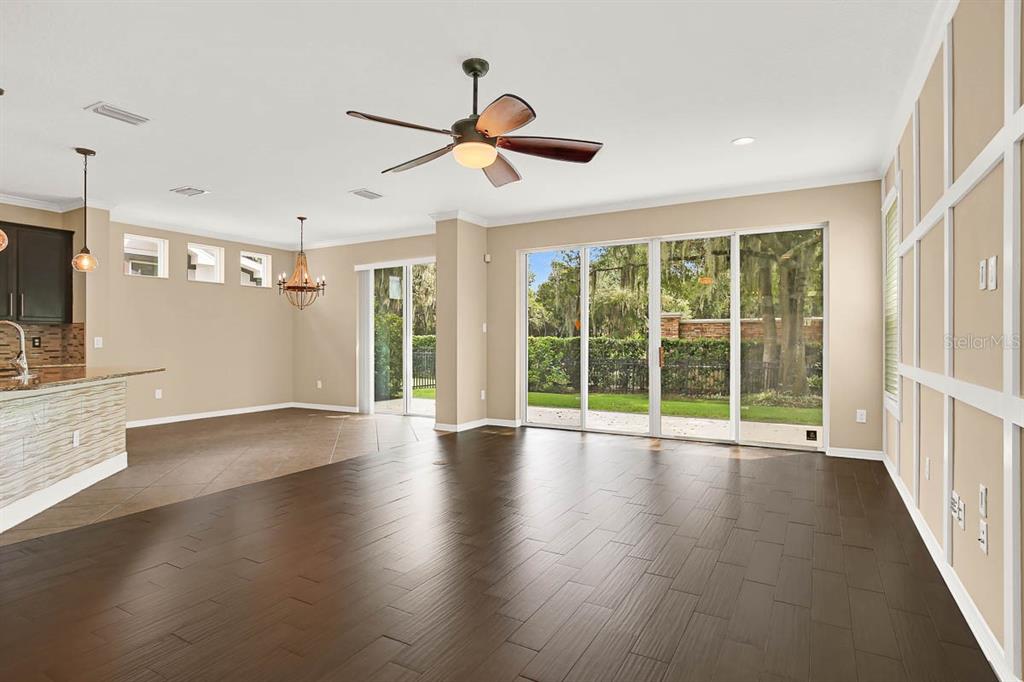 An open-concept living area with dark wood flooring, a ceiling fan, and sliding glass doors — 16405 EGRET CROSSING LANE, LITHIA, FL
