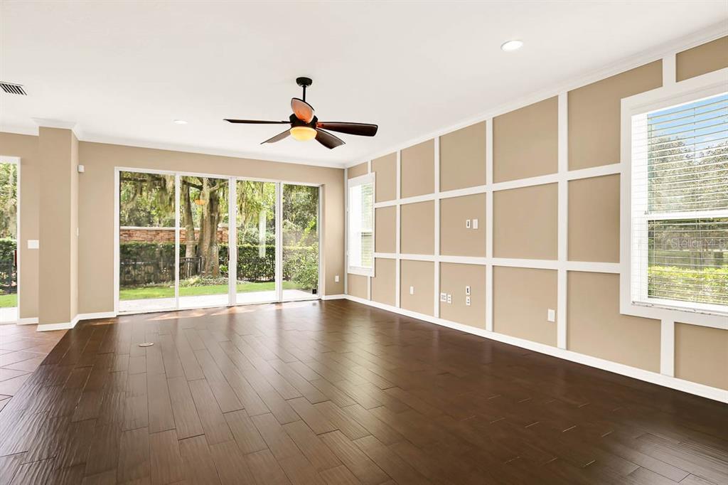 A spacious living room features dark wood flooring, a grid-patterned accent wall, and sliding glass doors — 16405 EGRET CROSSING LANE, LITHIA, FL