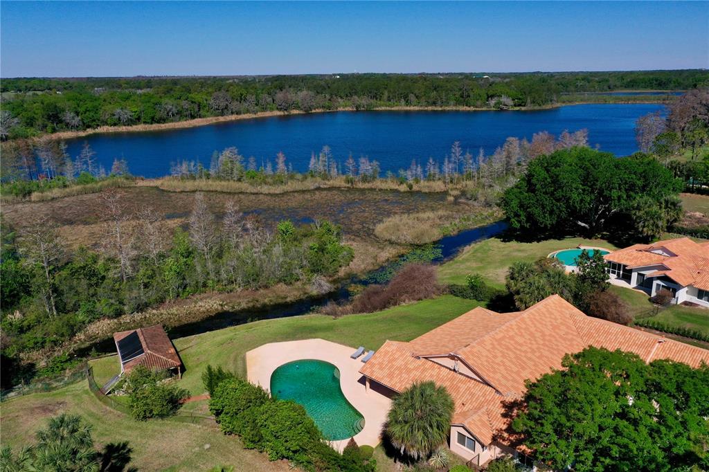An aerial view shows a house with a pool, a pond, and surrounding greenery — 12811 BELLERIVE DRIVE, CLERMONT, FL