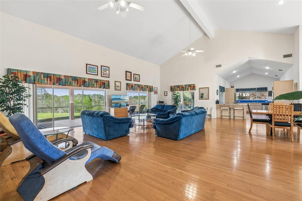 A spacious living room with hardwood floors, vaulted ceilings, blue furniture, and a dining area — 12811 BELLERIVE DRIVE, CLERMONT, FL