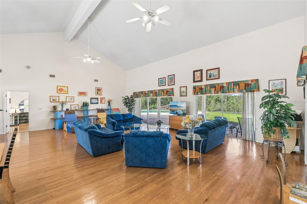 A spacious living room features vaulted ceilings, hardwood floors, blue furniture, and large glass doors — 12811 BELLERIVE DRIVE, CLERMONT, FL