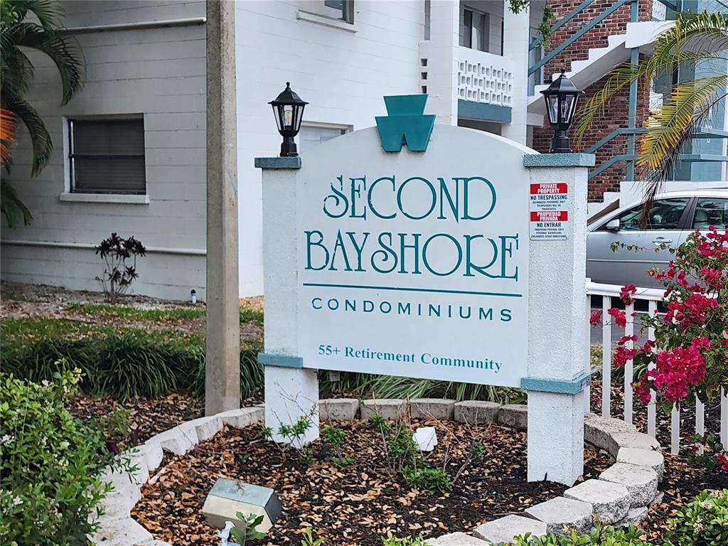 A sign for Second Bayshore Condominiums stands in a landscaped garden area — 5842 WELCOME ROAD UNIT J2, BRADENTON, FL