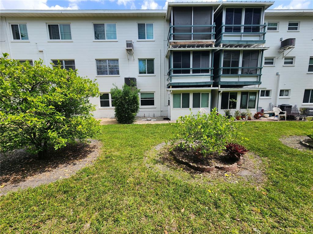 The exterior of a multi-story apartment building features a lawn with two small trees — 5842 WELCOME ROAD UNIT J2, BRADENTON, FL