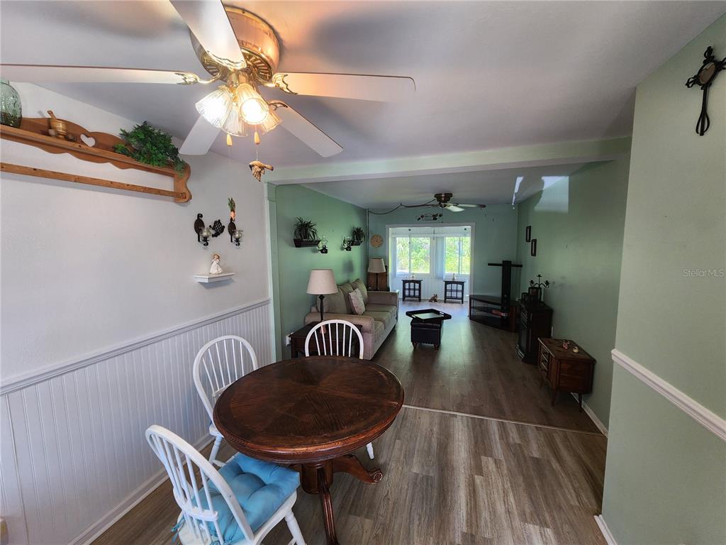 A dining area with a round wooden table opens into a living room with green walls — 5842 WELCOME ROAD UNIT J2, BRADENTON, FL
