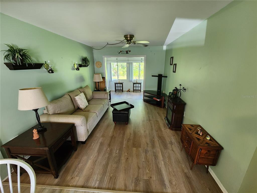 A living room features light green walls, wood-look flooring, a sofa, and a ceiling fan — 5842 WELCOME ROAD UNIT J2, BRADENTON, FL