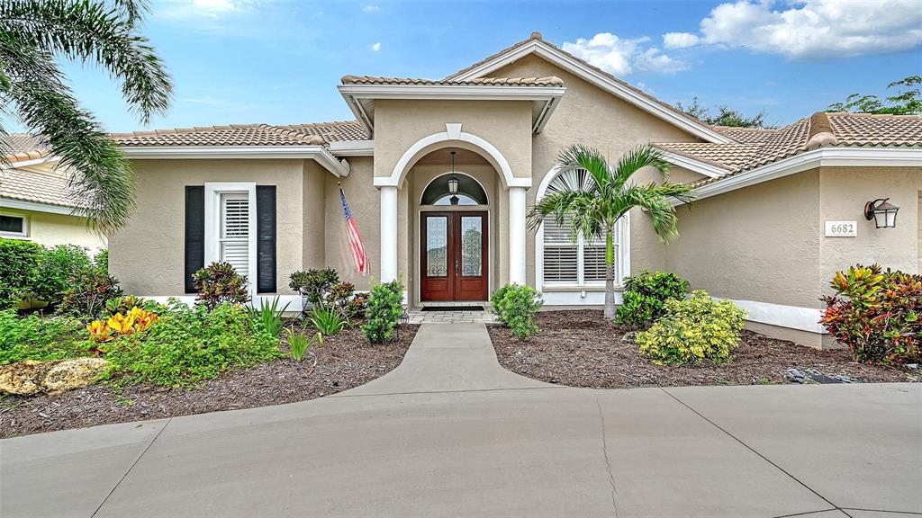A beige single-story house features a tiled roof, arched entryway, and a concrete driveway — 6682 SAINT JAMES CROSSING, UNIVERSITY PARK, FL