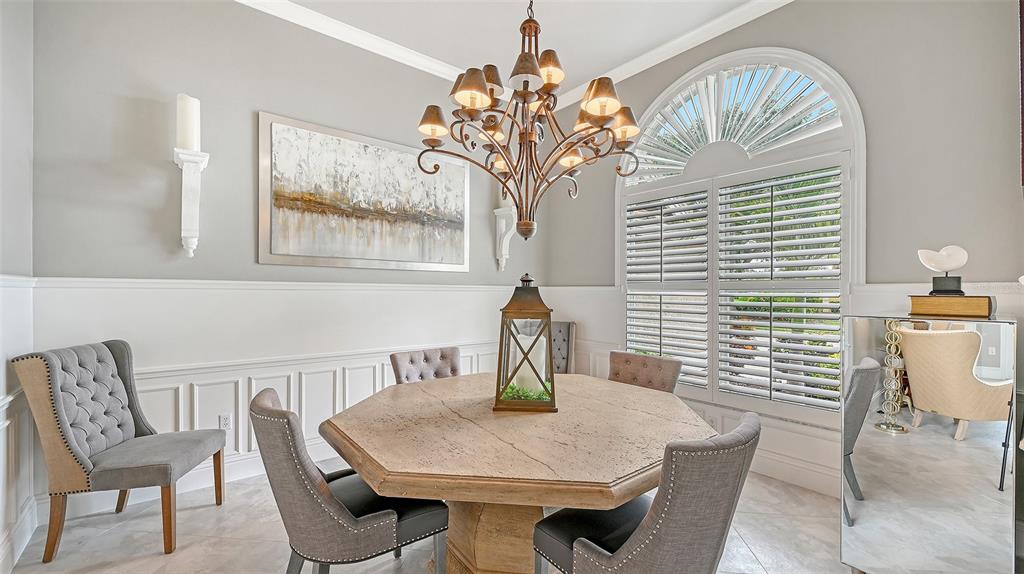 A dining room features an octagonal stone table, gray upholstered chairs, and a large chandelier — 6682 SAINT JAMES CROSSING, UNIVERSITY PARK, FL