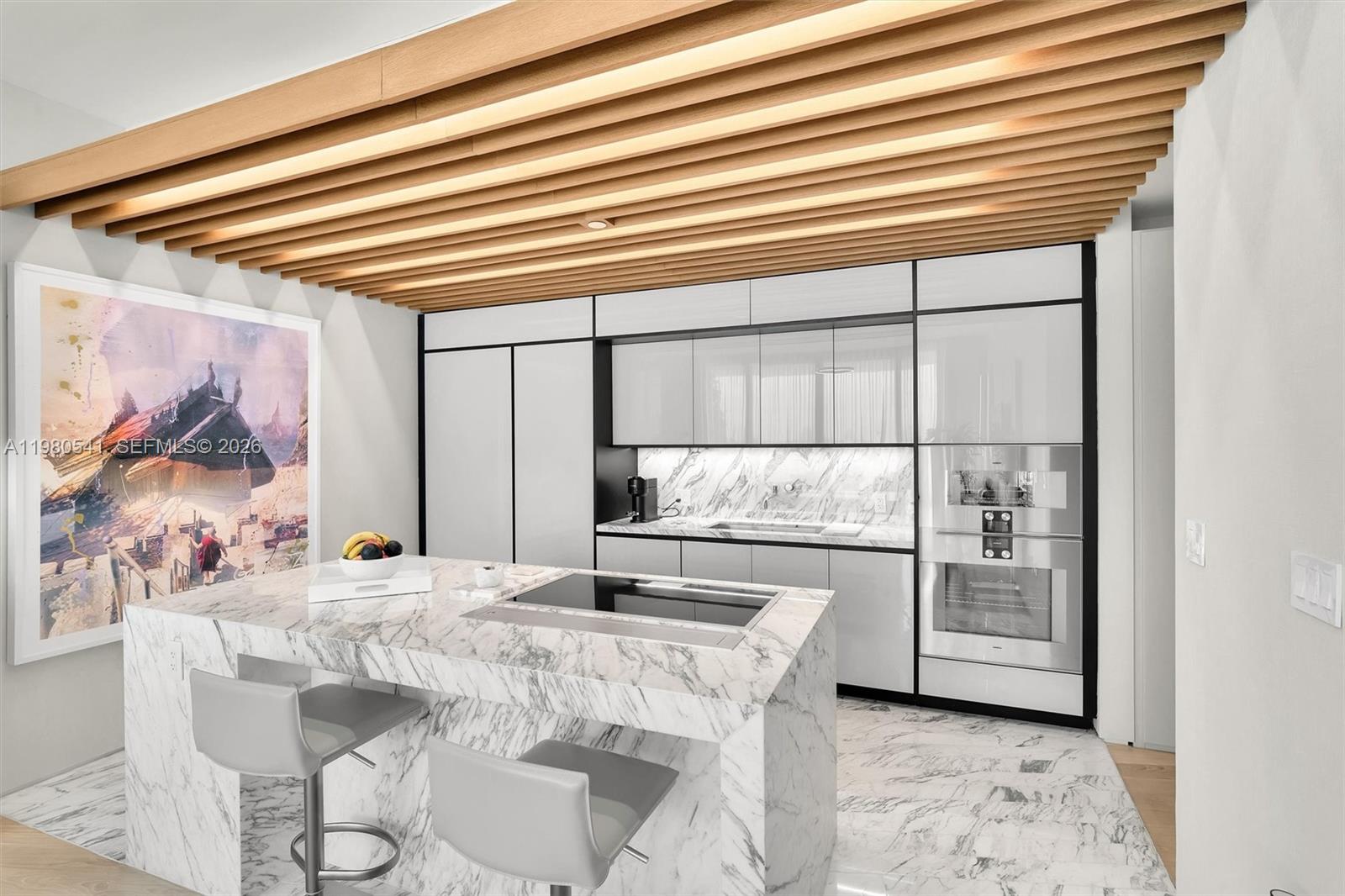 A modern kitchen features a marble island, white cabinetry, and a slatted wood ceiling — 1300 Monad Ter # 7C, Miami Beach FL 33139, MIAMI BEACH, FL