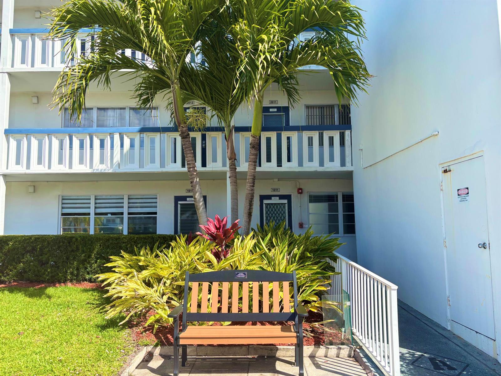 A bench sits in front of a two-story apartment building with palm trees and landscaping — 4015 Oakridge A # 4015, Deerfield Beach FL 33442, DEERFIELD BEACH, FL