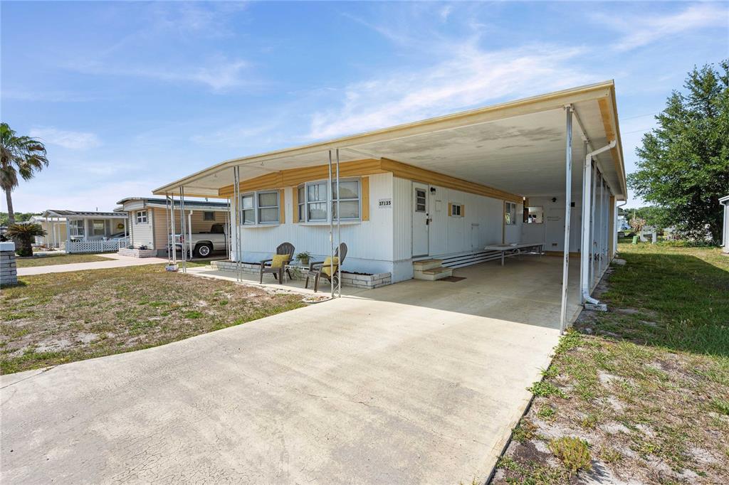 A single-story manufactured home features a white exterior, yellow trim, and an attached carport — 37135 SANDRA AVENUE, ZEPHYRHILLS, FL