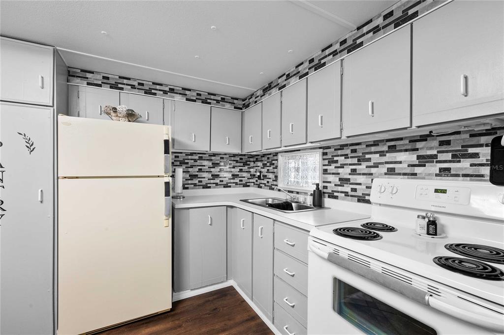 A kitchen features grey cabinets, a white refrigerator, a white stove, and a tiled backsplash — 37135 SANDRA AVENUE, ZEPHYRHILLS, FL