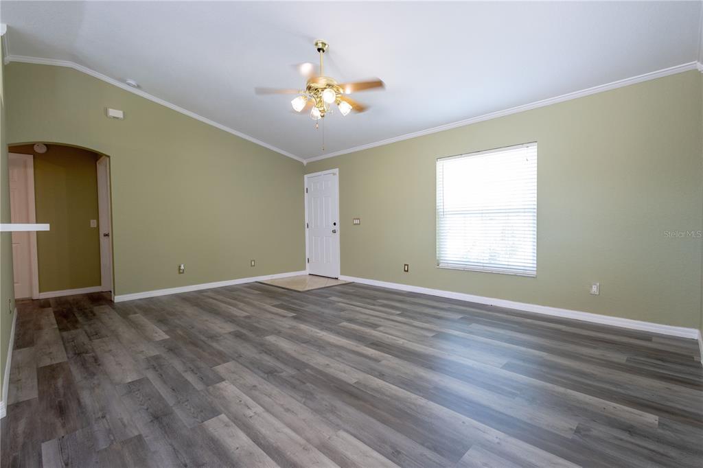 An empty living room features light green walls, gray wood-look flooring, and a ceiling fan — 25324 LYCHEE COURT, PUNTA GORDA, FL