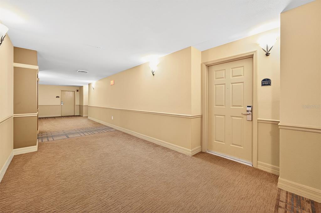 A carpeted apartment building hallway features beige walls, chair rail molding, and unit door 5901 — 8125 RESORT VILLAGE DRIVE UNIT 5901, ORLANDO, FL