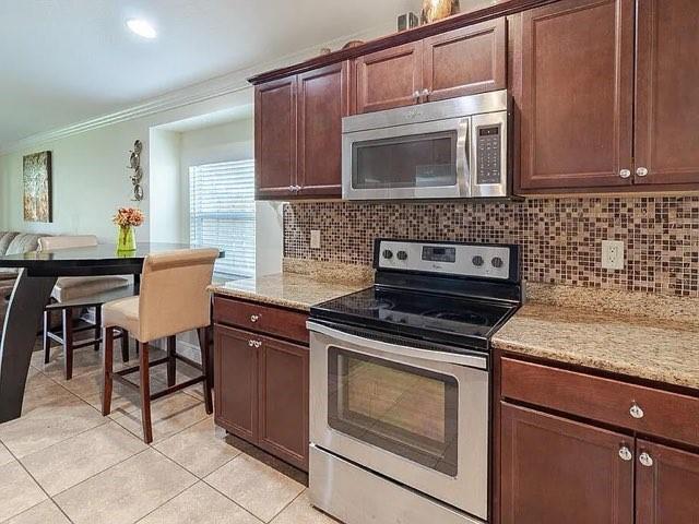 A kitchen features dark wood cabinets, stainless steel appliances, and a mosaic tile backsplash — 9446 Windrift Circle, Fort Pierce FL 34945, FORT PIERCE, FL