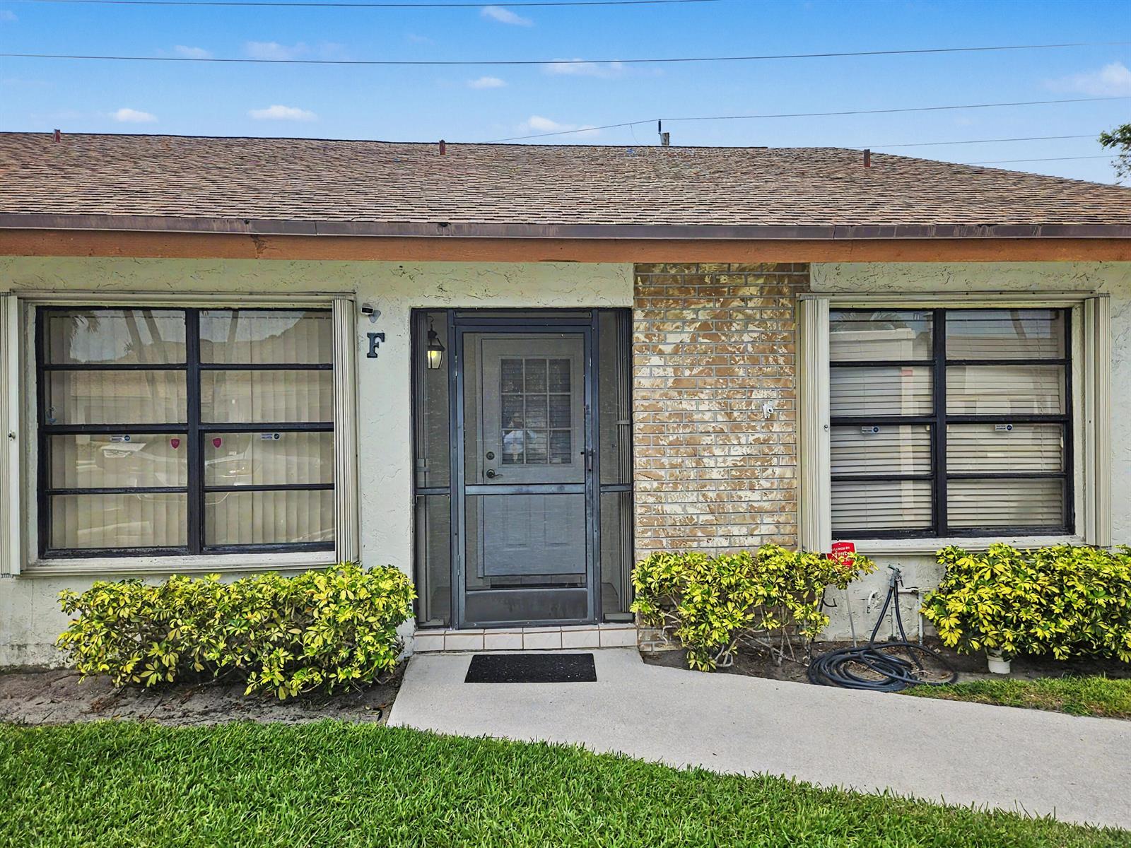 The exterior of a single-story home features a brick accent wall and a screen door — 1160 Parkside Green Drive # F, FL 33415, FL