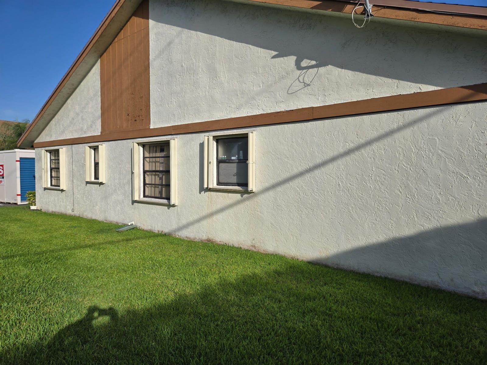 The exterior side of a house features a stucco wall, brown trim, and four windows — 1160 Parkside Green Drive # F, FL 33415, FL