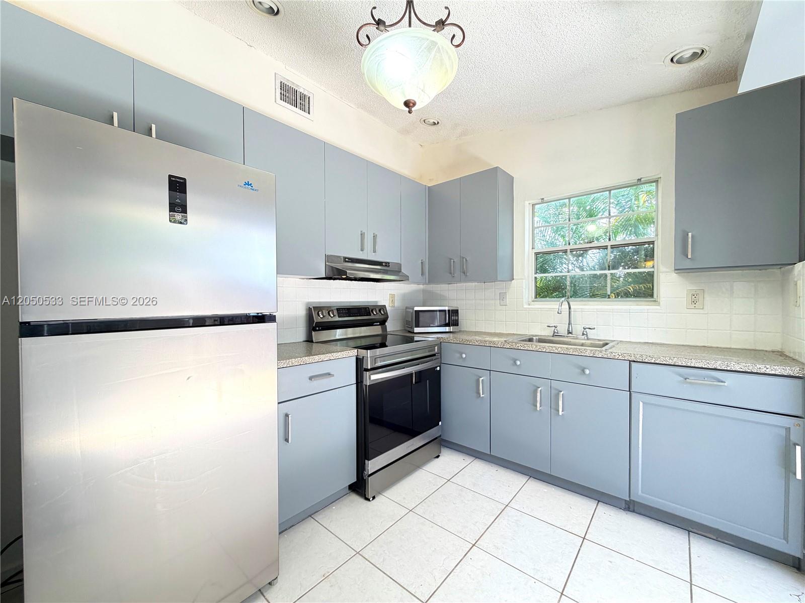 A kitchen features light blue cabinets, stainless steel appliances, and white tiled floors — 9850 W Heather Ln, Miramar FL 33025, MIRAMAR, FL