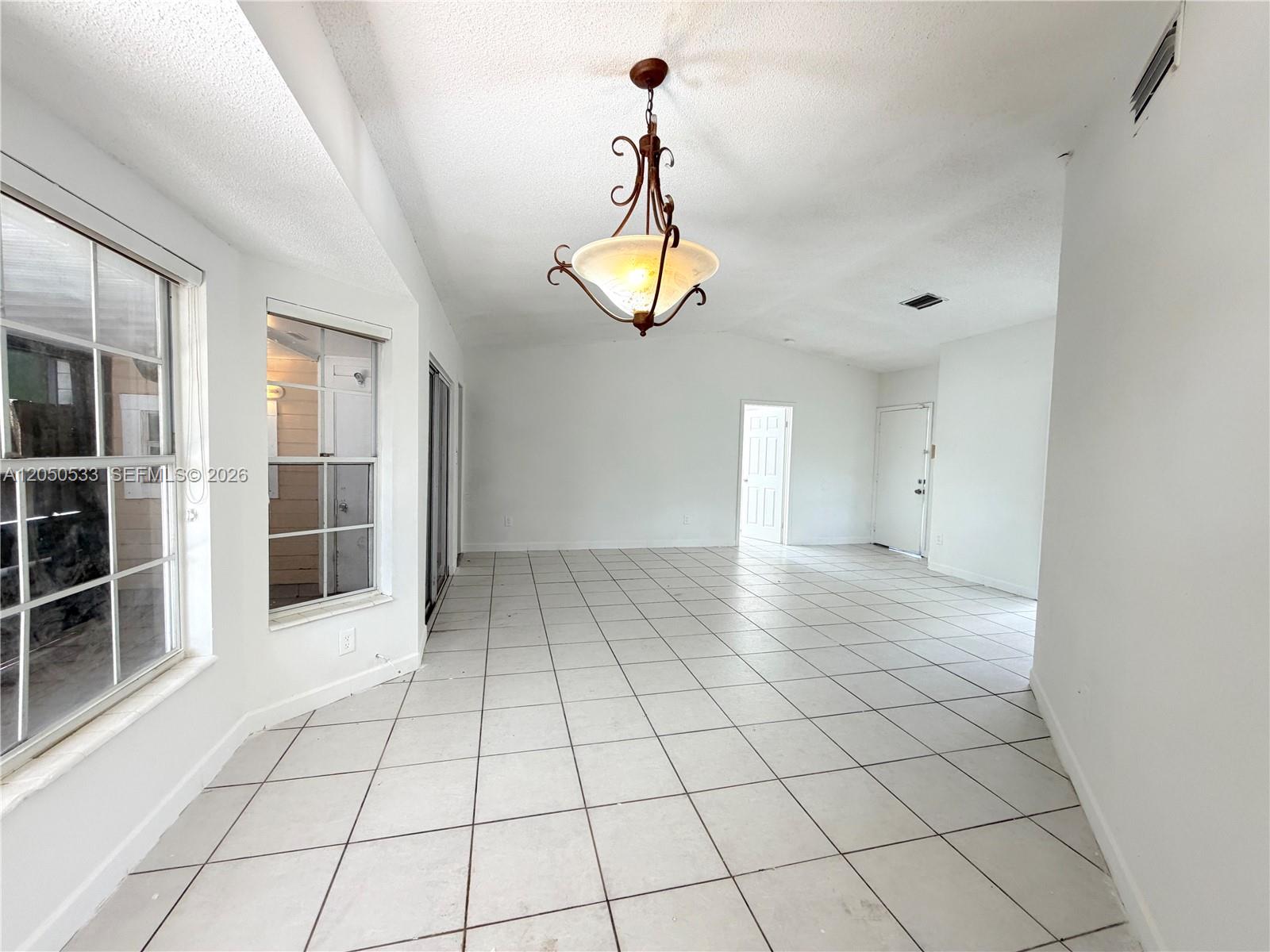 An empty room features white tiled floors, a vaulted ceiling, and a decorative chandelier — 9850 W Heather Ln, Miramar FL 33025, MIRAMAR, FL