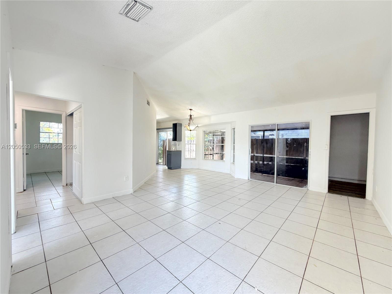 A bright, open-concept living area features white tile flooring, vaulted ceilings, and sliding glass doors — 9850 W Heather Ln, Miramar FL 33025, MIRAMAR, FL