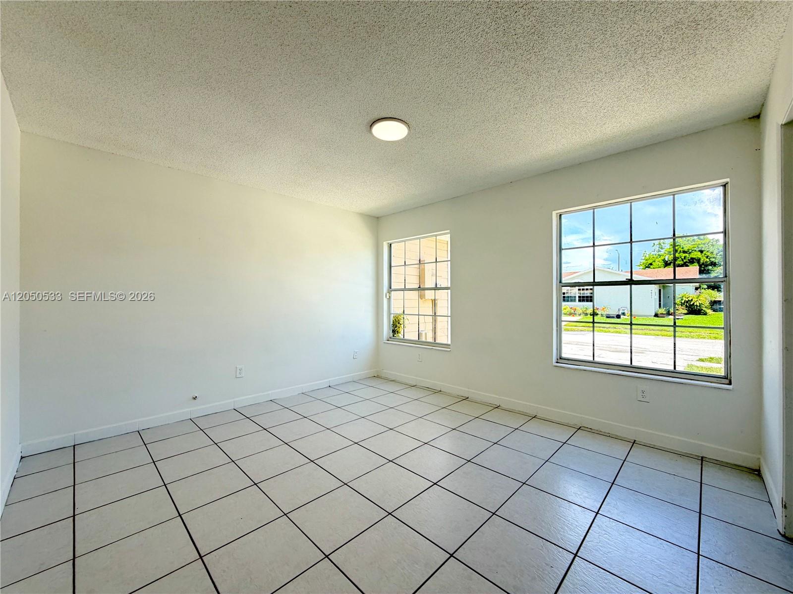 An empty room features white walls, a popcorn ceiling, and light-colored square floor tiles — 9850 W Heather Ln, Miramar FL 33025, MIRAMAR, FL