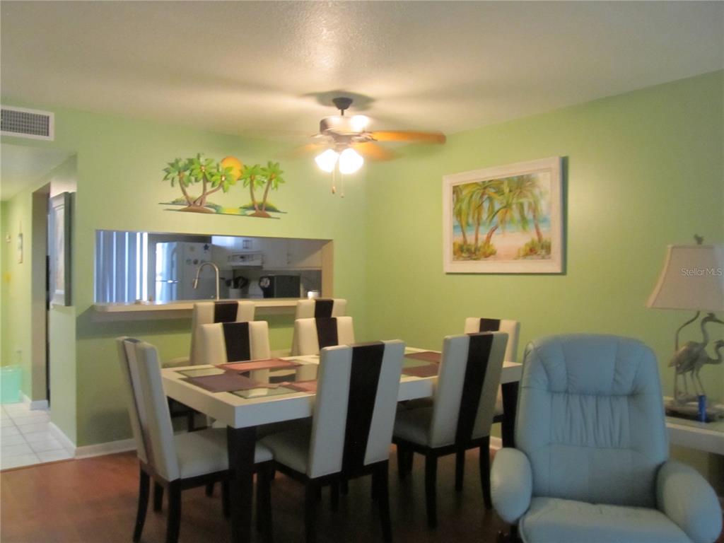 A dining area with a table, chairs, light green walls, and a kitchen pass-through window — 4733 WINSLOW BEACON UNIT 13, SARASOTA, FL