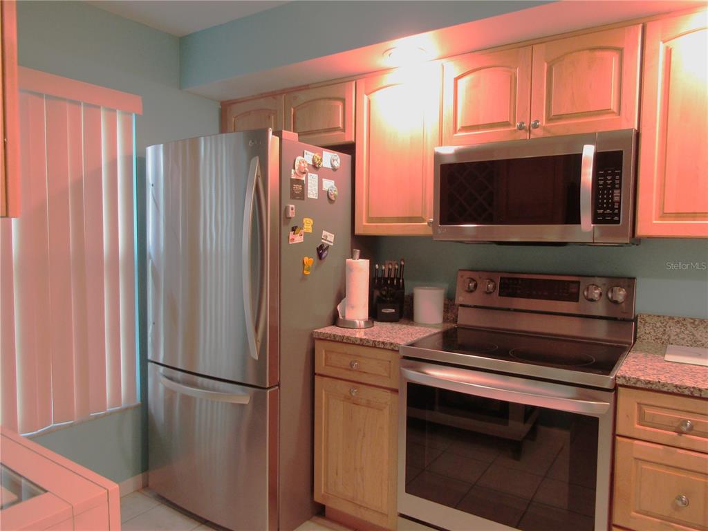 A kitchen features stainless steel appliances, light wood cabinets, and granite countertops — 4733 WINSLOW BEACON UNIT 13, SARASOTA, FL