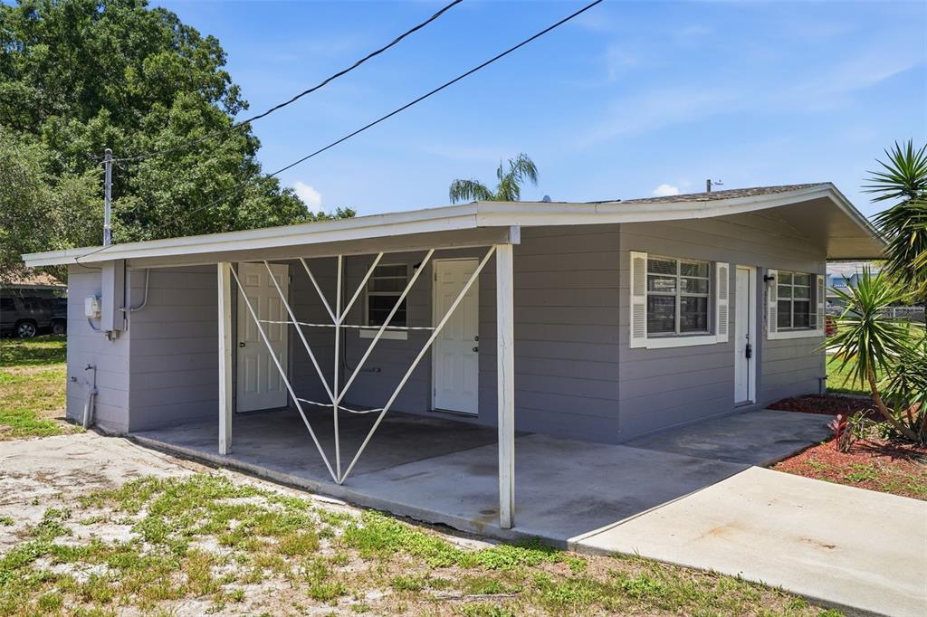 A gray, single-story house features a covered carport with decorative metal supports and two doors — 3214 AVENUE Q NW, WINTER HAVEN, FL