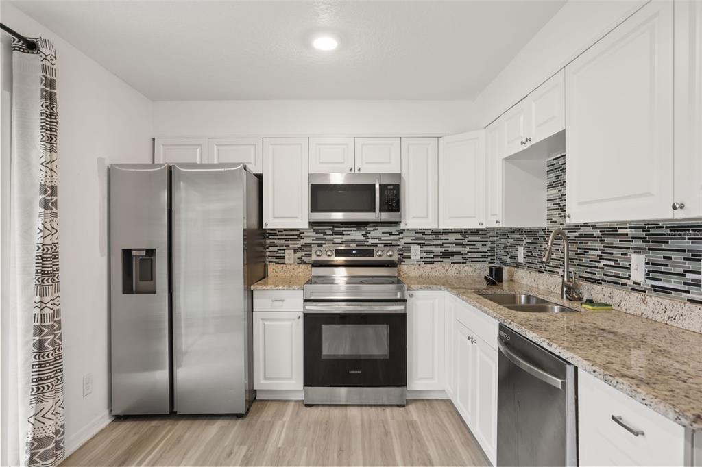 A kitchen with white cabinets, stainless steel appliances, granite countertops, and a mosaic tile backsplash — 4650 BOCA VISTA COURT, ORLANDO, FL