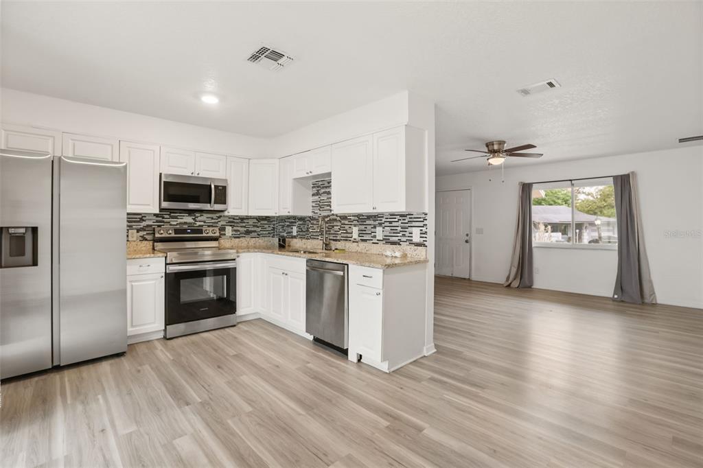 A kitchen with white cabinets, stainless steel appliances, and light wood-look flooring — 4650 BOCA VISTA COURT, ORLANDO, FL