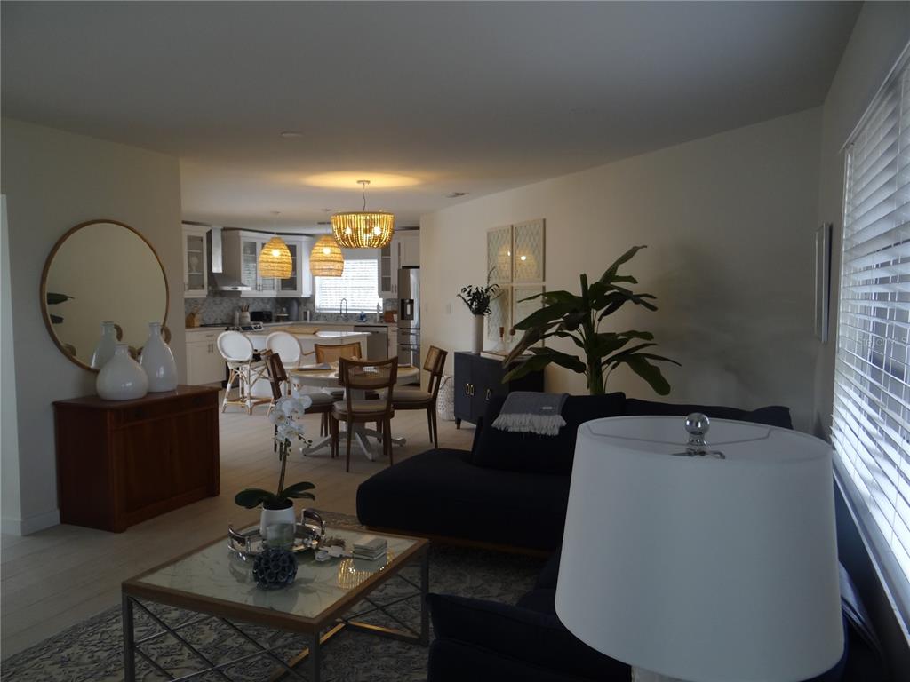 An open-concept living and dining area features a dark sofa, round mirror, and kitchen island — 2473 ROSA LANE, PUNTA GORDA, FL
