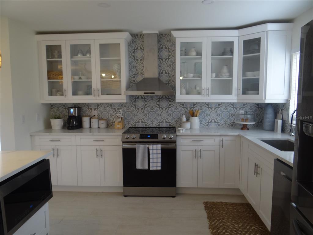 A kitchen with white cabinets, patterned tile backsplash, stainless steel appliances, and light flooring — 2473 ROSA LANE, PUNTA GORDA, FL